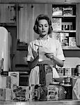 1960s WOMAN HOUSEWIFE IN KITCHEN CHECKING GROCERY FOOD SHOPPING LIST