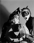 1950s TWO CHILDREN IN HALLOWEEN COSTUME BEHIND A CARVED PUMPKIN JACK-O-LANTERN