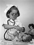 1950s - 1960s GIRL WEARING NURSE UNIFORM EYEGLASSES PUTTING BANDAGE ON DOLL'S ARM