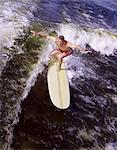 1950s - 1960s YOUNG MAN RED SWIM TRUNKS YELLOW SURFBOARD RIDING A WAVE SURFING
