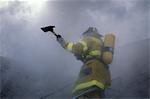 FIREMAN WITH FIRE AX WORKING IN DENSE SMOKE STANDING ON LADDER AT A HOUSE FIRE