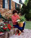1980s WOMAN PLANTING GERANIUMS IN TERRA COTTA POT