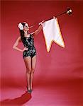 1960s YOUNG WOMAN IN SEQUINED BLACK SWIMSUIT BLOWING BAROQUE TRUMPET WITH PENNANT