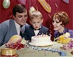 1960s - 1970s FAMILY FATHER AND MOTHER WITH SON AND BIRTHDAY CAKE WITH CANDLES