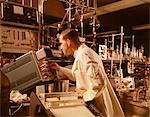 1960s SCIENTIST LAB TECHNICIAN LOOKING INTO OSCILLOSCOPE IN LABORATORY