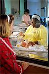 NURSE IN HOSPITAL NURSERY SHOWING BABY TO MOTHER THROUGH WINDOW