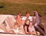 1960ER JAHRE FAMILIE SITZEND LÄCHELND IN OFFENEN WEIßEN CABRIO AUTOMOBILE