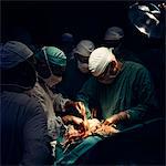 1960s DOCTORS AND NURSES IN SURGERY OPERATING THEATER PERFORMING MEDICAL PROCEDURE