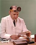 1960s MAN DOCTOR SEATED AT DESK READING PAPERWORK