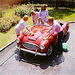 1970s FOUR TEENAGERS WASHING RED AUSTIN HEALEY SPORTS CONVERTIBLE AUTOMOBILE MAN WOMAN OVERHEAD OUTDOOR