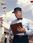 1950s - 1960s MAN SERVICE MANAGER AT AUTOMOBILE GAS AND REPAIR SERVICE STATION WRITING ON CLIPBOARD
