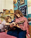 1980s TWO TEEN GIRLS SITTING BED DORMITORY ROOM PLAYING GUITAR