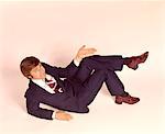 1970s OVERHEAD LOOKING DOWN AT MAN LYING DOWN LEGS CROSSED WEARING BUSINESS SUIT SHRUG OFF HAND EXPRESSION