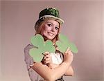 1960s - 1970s IRISH WOMAN SMILING HOLDING GREEN SHAMROCKS AND WEARING GREEN PARTY HAT