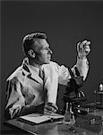 1950s MAN SCIENTIST HOLDING TEST TUBE MAKING NOTES BY MICROSCOPE