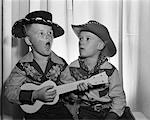 1950s 2 JUVENILE BOYS IN COWBOY HAT & SHIRTS PLAYING UKULELE & SINGING MOUTH OPEN WIDE