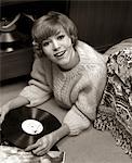 ANNÉES 1960 SOURIANTE JEUNE FEMME PULL SITUÉE À L'ÉTAGE CHAMBRE ÉCOUTER DE LA MUSIQUE SUR VINYL RECORD ALBUM