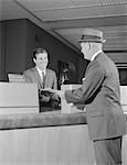 1960s BUSINESSMAN MAKING A DEPOSIT INTO SAVINGS ACCOUNT WITH BANK TELLER