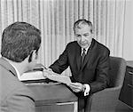 1960s - 1970s MAN FROM BEHIND MEETING AT DESK OF OLDER BUSINESSMAN