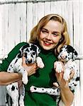 1950s PORTRAIT SMILING TEEN GIRL WEARING GREEN SWEATER HOLDING TWO DALMATIAN PUPPIES
