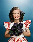 1940s - 1950s SMILING YOUNG WOMAN WEARING RED AND WHITE DRESS HOLDING BOUQUET OF VIOLETS