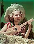 1940s - 1950s SMILING BLOND WOMAN WEARING STRAW HAT SITTING ON HAY PLAYING UKULELE