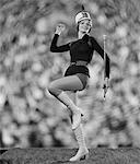 1970s SMILING YOUNG WOMAN MAJORETTE WHITE BOOTS HOT PANTS MARCHING