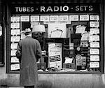 1940s MAN LOOKING AT WINDOW DISPLAY OF RADIOS ON SALE IN NEW YORK CITY