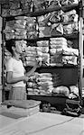 1940s ASIAN MAN HAND CHINESE LAUNDRY LOOKING AT SHELVES OF LAUNDRY WRAPPED IN BROWN PAPER