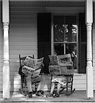 ANNÉES 1950 - ANNÉES 1960 COUPLE HOMME FEMME ASSISE SUR PORCHE DANS ROCKING CHAISES BRANDISSANT LA CACHER LEURS VISAGES DE JOURNAUX