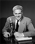 1950s SMILING MAN RADIO ANNOUNCER NEWSCASTER SITTING SPEAKING AT MICROPHONE STUDIO INDOOR