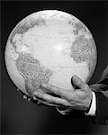 1960s MANS HAND HOLDING GLOBE OF THE WORLD