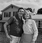 1960s HAPPY COUPLE PORTRAIT MAN WOMAN SMILING IN FRONT OF HOME