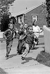 1950s GROUP OF SCHOOL CHILDREN RUNNING AROUND CORNER OF PICKET FENCE IN SUBURBAN NEIGHBORHOOD