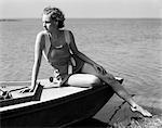 1930s WOMAN WEARING ONE PIECE BATHING SUIT SITTING ON EDGE OF BOAT