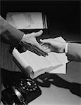 1950s CLOSE-UP TWO MALE HANDS ABOUT TO SHAKE OVER DESK WITH PAPERS AND TELEPHONE