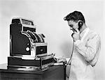 1930s - 1940s MAN IN APRON NEXT TO LARGE CASH REGISTER TALKING ON PHONE TAKING NOTES SMILING