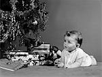 1940s BABY LAYING IN FRONT OF CHRISTMAS TREE AND CHRISTMAS PRESENTS