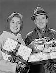 1960s COUPLE MAN AND WOMAN HOLDING WRAPPED CHRISTMAS PRESENTS AND PACKAGES