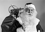 1960s PORTRAIT OF SMILING SANTA CLAUS WITH SACK OF CHRISTMAS TOY PRESENTS SLUNG OVER HIS SHOULDER