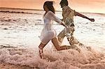 Couple en cours d'exécution dans les vagues à la plage