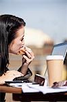Jeune femme mangeant un sandwich tout en utilisant un ordinateur portable