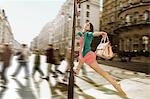 Mid adult woman in pink dress leaping through city streets
