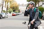 Mid adult businessman using cellphone on bicycle