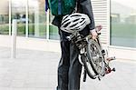 Mid adult businessman carrying folding bicycle