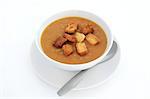 Lentil soup with croutons in a white porcelain bowl with plate and spoon isolated over white background.