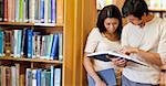 Smiling students looking at a book in a library