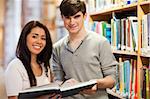 Happy students holding a book in a library