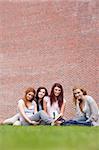 Portrait of friends posing with a book while sitting on the lawn