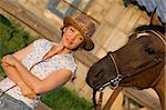 Woman in hat staying above brown horse